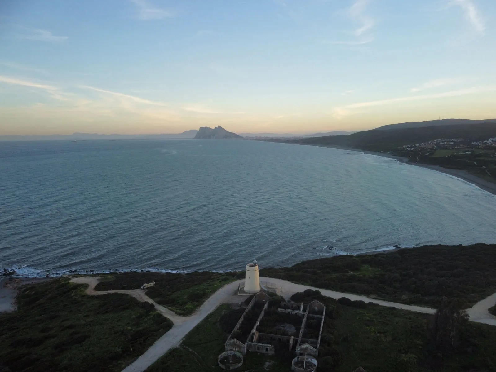 A lighthouse on the coast at sunset with the Rock of Gibraltar on the horizon